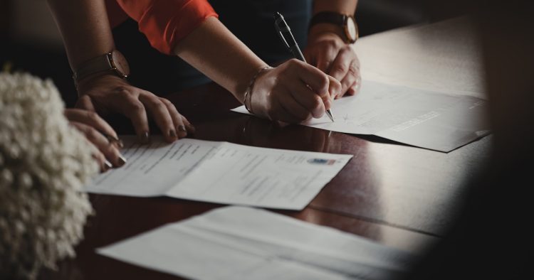 Hands signing school forms and paperwork at a desk with a pen