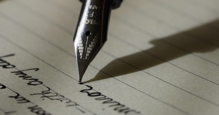 A teacher writing a college recommendation letter with a fountain pen