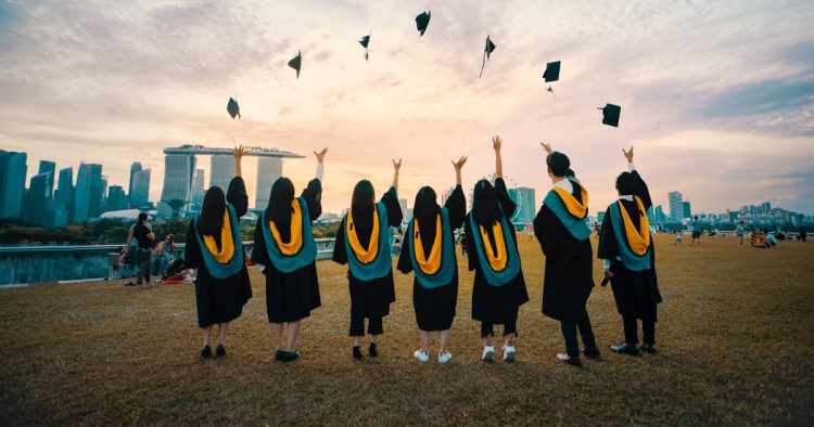 一群戴學士帽的畢業生在夕陽下拋帽慶祝，象徵美國大學錄取結果