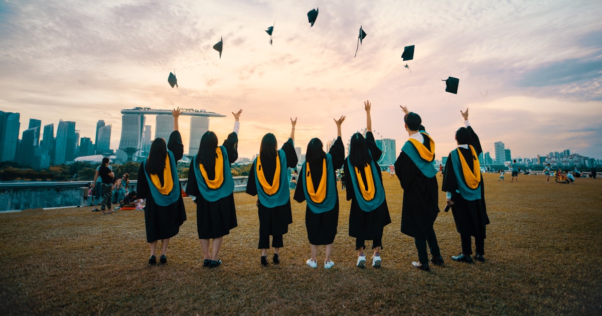 一群戴學士帽的畢業生在夕陽下拋帽慶祝，象徵美國大學錄取結果